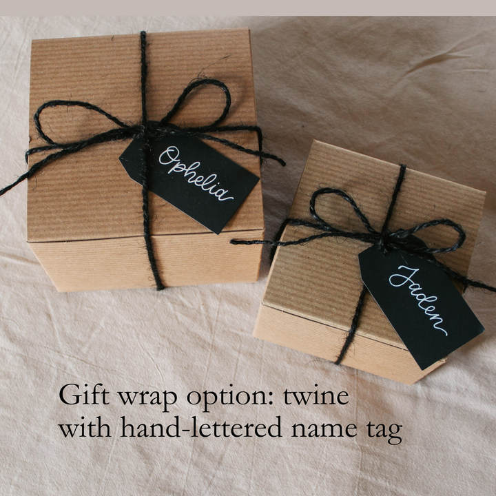 two kraft gift boxes wrapped in black twine, and black gift tags with white lettering demonstrating the way the gift boxes will look if you choose the twin and name tag option.
