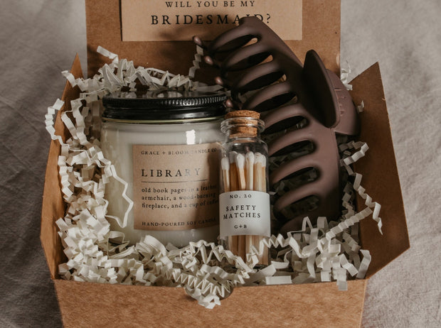 Say "Will you be my bridesmaid?" in style with this dark academia bridesmaid proposal gift box! Show your favorite bookish friends how much you appreciate their help with this thoughtful combo, featuring one Grace + Bloom literary-themed candle for them to light while they read, a decorative glass bottle of white-tipped matches, a cute claw clip to keep their hair back, and a custom-designed "Will you be my..." card that doubles as a bookmark