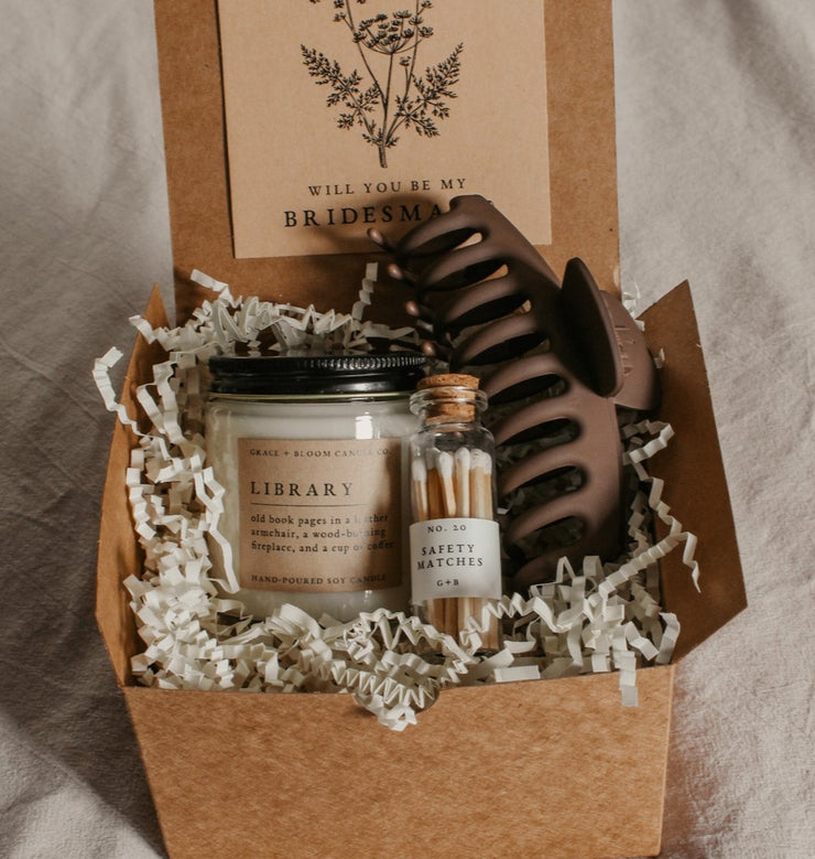 Say "Will you be my bridesmaid?" in style with this dark academia bridesmaid proposal gift box! Show your favorite bookish friends how much you appreciate their help with this thoughtful combo, featuring one Grace + Bloom literary-themed candle for them to light while they read, a decorative glass bottle of white-tipped matches, a cute claw clip to keep their hair back, and a custom-designed "Will you be my..." card that doubles as a bookmark