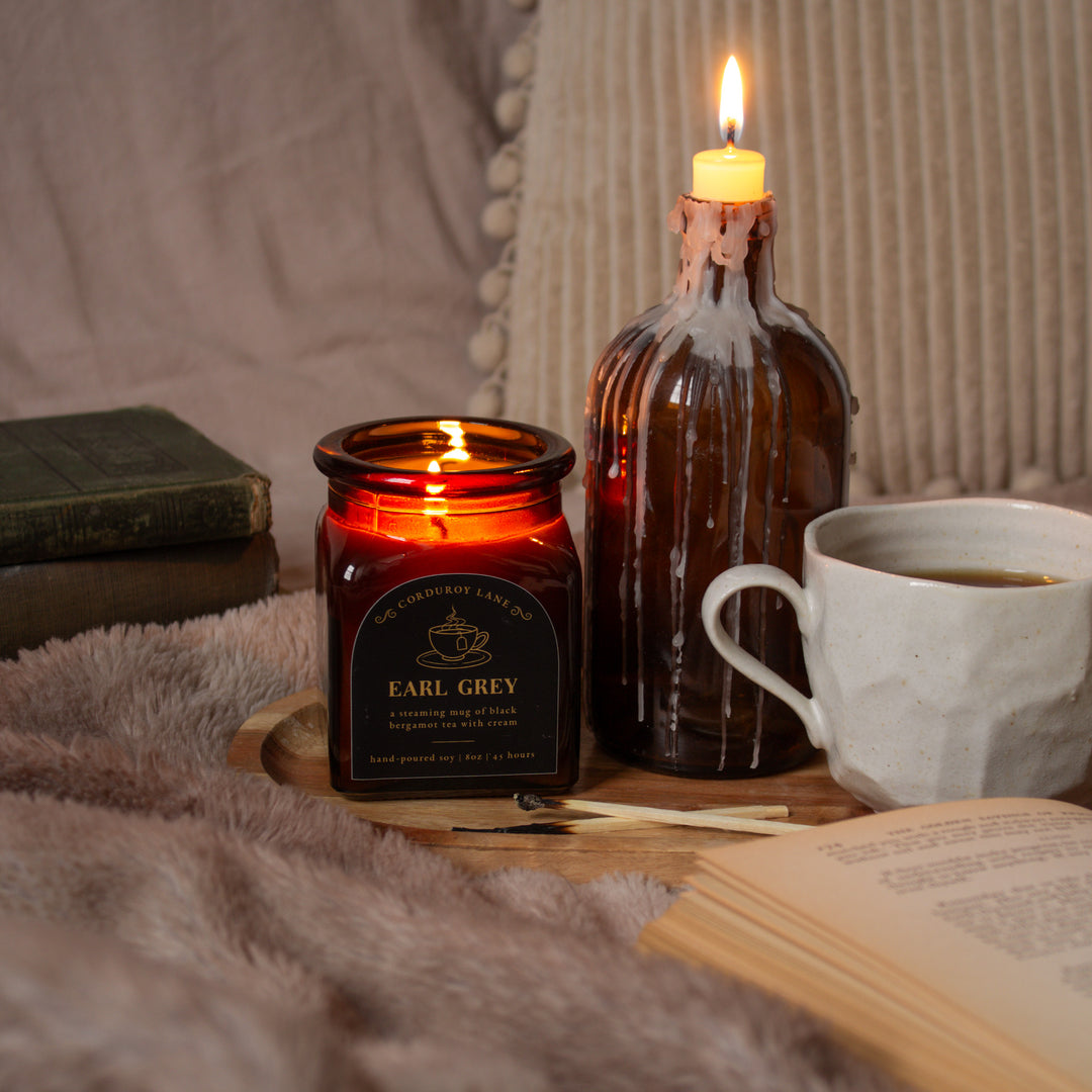 Candle and cup of tea on a wooden surface with a soft blanket and book in the background