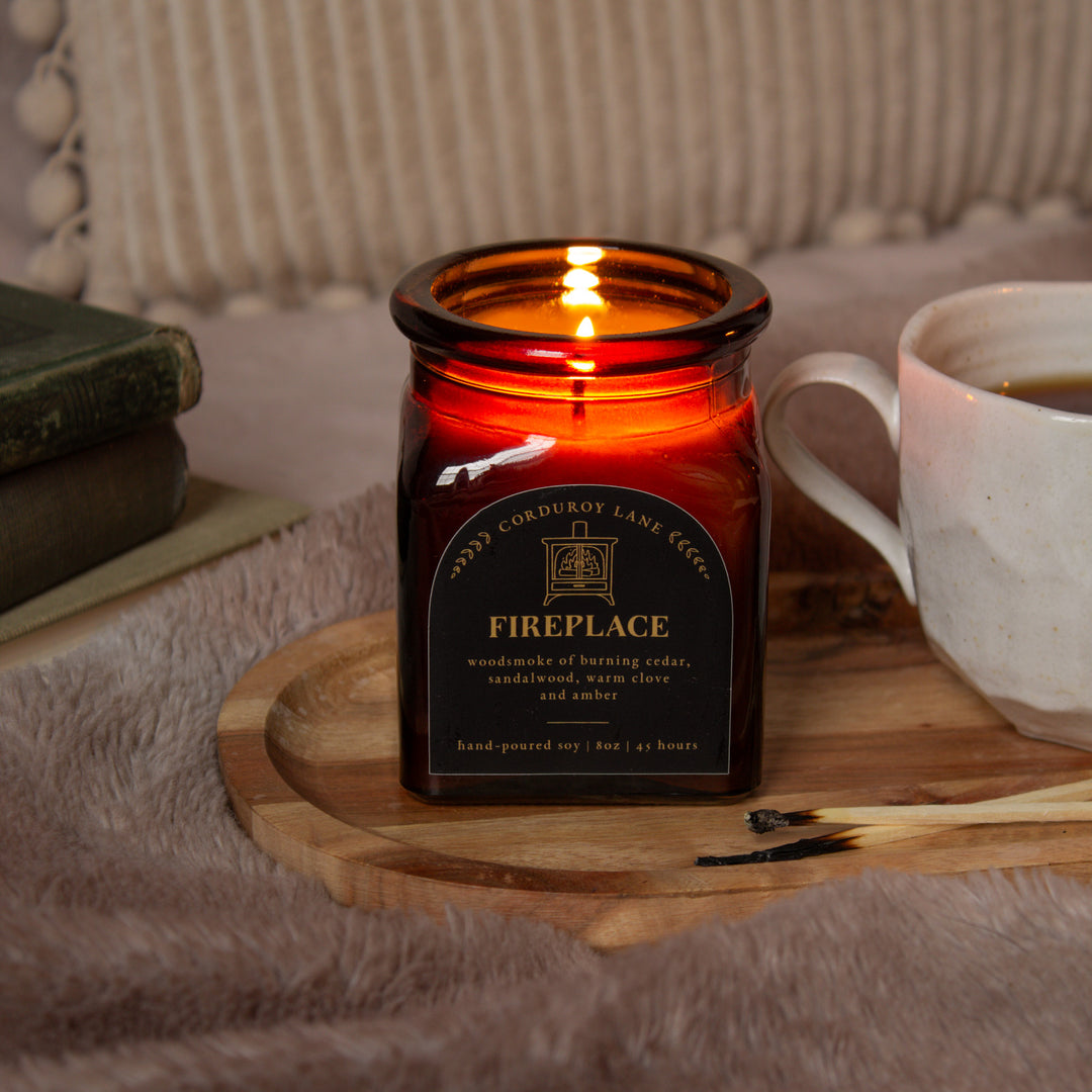 Candle labeled 'Fireplace' in a decorative setting with a mug and books.