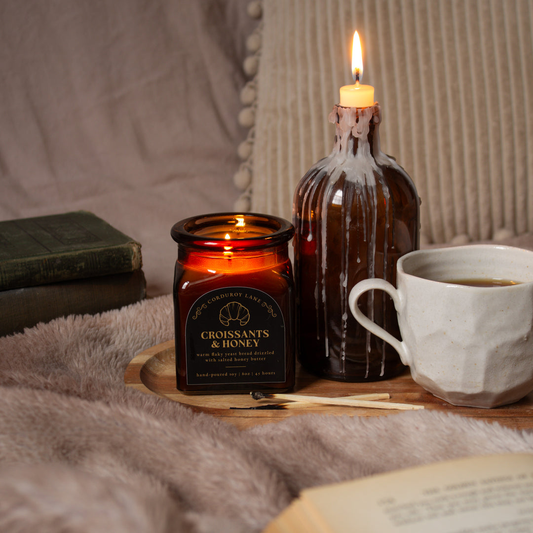 Candle and mug on a wooden tray with books and a blanket in the background