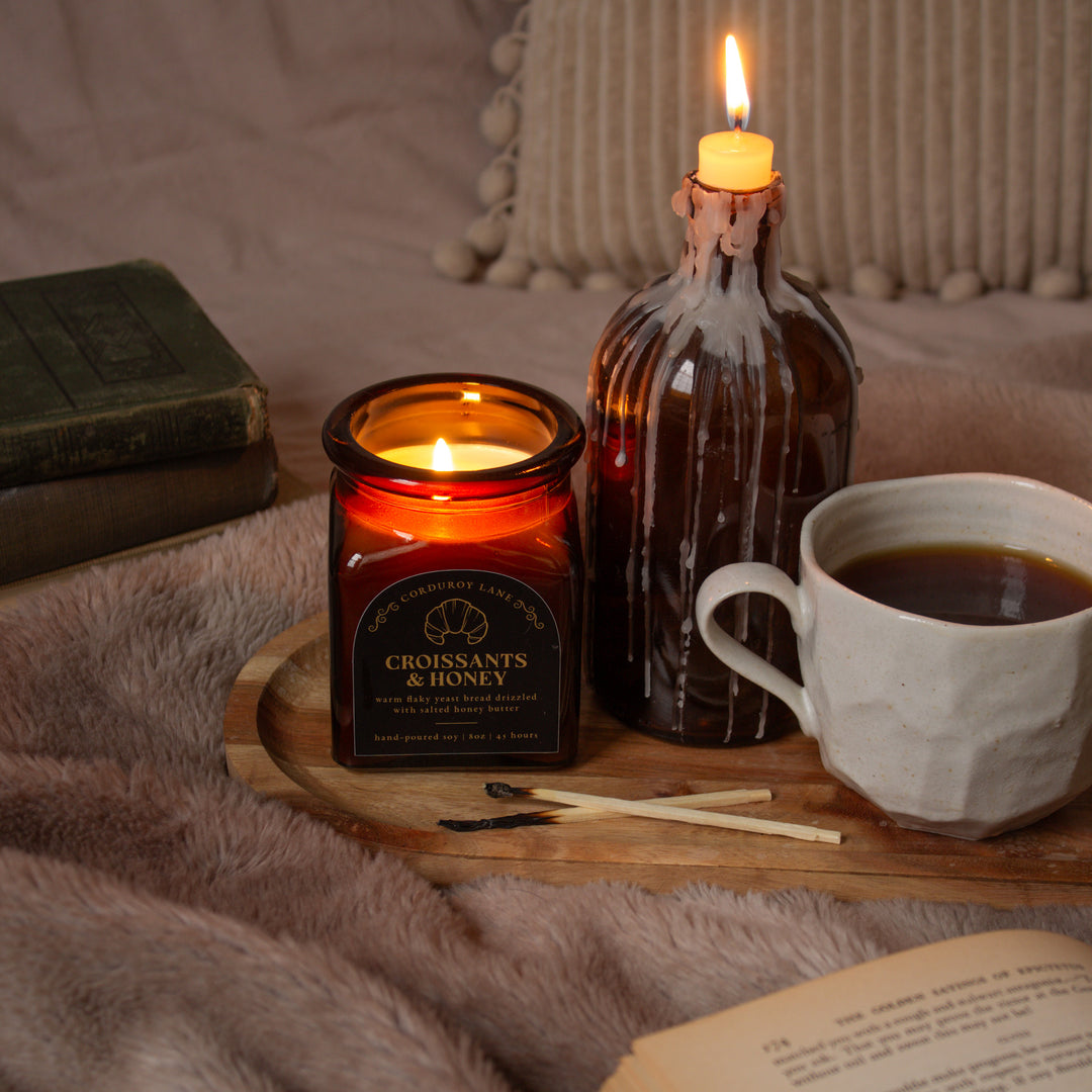 Candle, cup of coffee, and bottle on a wooden tray with a soft blanket background