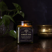 Forest Fog: a cozy spooky candle from Corduroy Lane in a green glass square apothecary jar with a cork lid and a black label, scented in a refreshing, masculine blend of misty ozone and woodlands with lavender, mint, and juniper for lovers of all things cozy and bookish