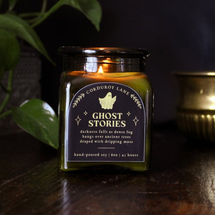 Ghost Stories: a spooky halloween candle from Corduroy Lane in a green glass square apothecary jar with a cork lid and a black and gold label, scented in a refreshing, masculine blend of misty ozone and woodlands with lavender, mint, and juniper for lovers of all things cozy and spooky