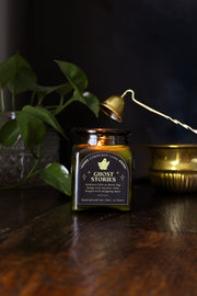 Ghost Stories: a spooky halloween candle from Corduroy Lane in a green glass square apothecary jar with a cork lid and a black and gold label, scented in a refreshing, masculine blend of misty ozone and woodlands with lavender, mint, and juniper for lovers of all things cozy and spooky