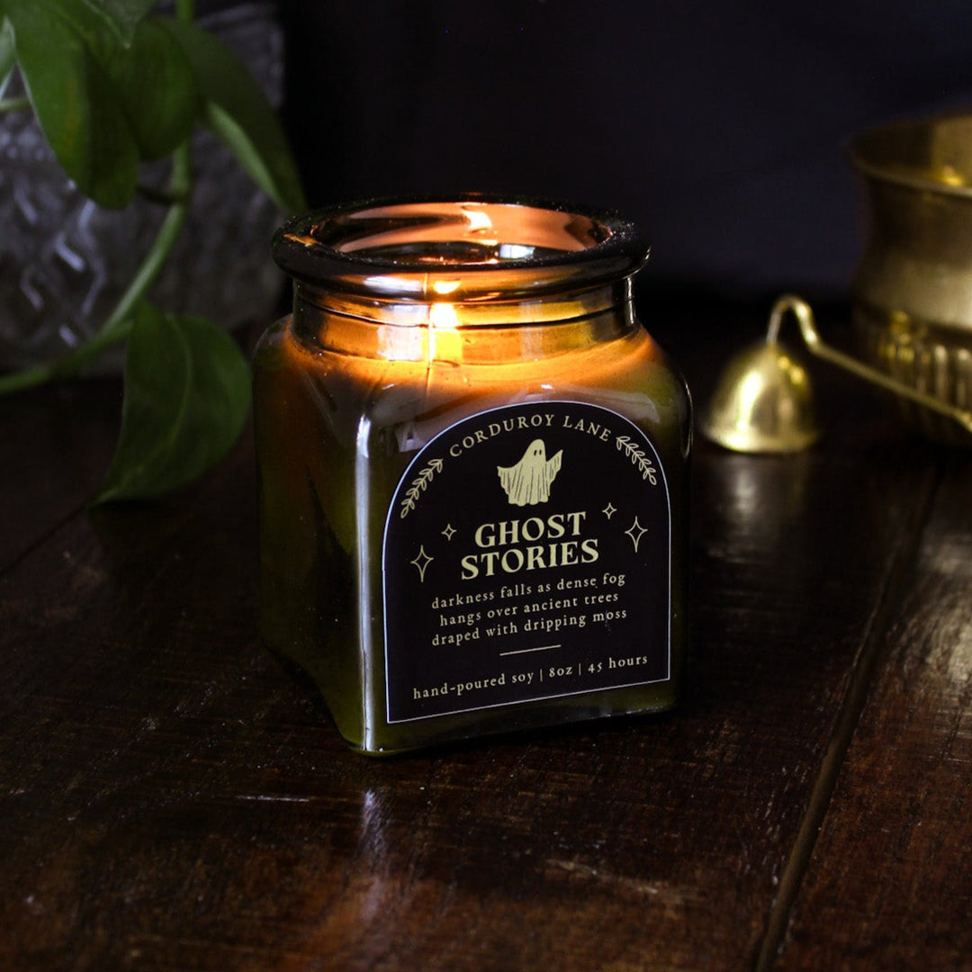 Ghost Stories: a spooky halloween candle from Corduroy Lane in a green glass square apothecary jar with a cork lid and a black and gold label, scented in a refreshing, masculine blend of misty ozone and woodlands with lavender, mint, and juniper for lovers of all things cozy and spooky