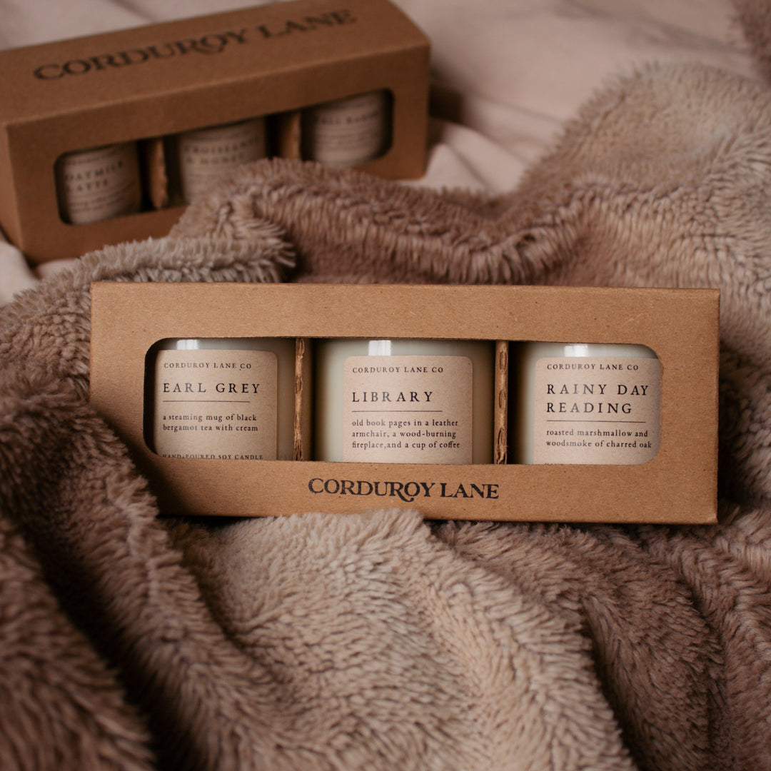 Three candles in a cardboard holder with 'Corduroy Lane' branding on a textured fabric background.