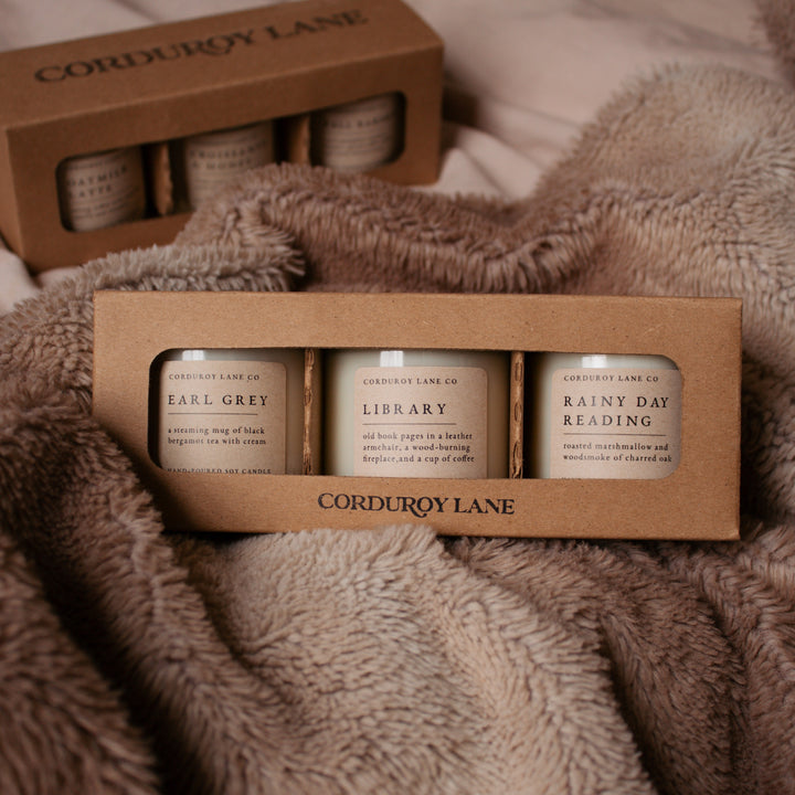 Three candles in a cardboard holder with 'Corduroy Lane' branding on a textured fabric background.