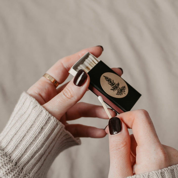 hands demonstrating how to use the striker pad on the side of a black matchbox.