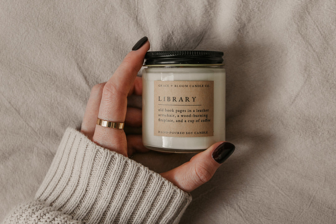 Hand holding a candle labeled 'Library' with a neutral background