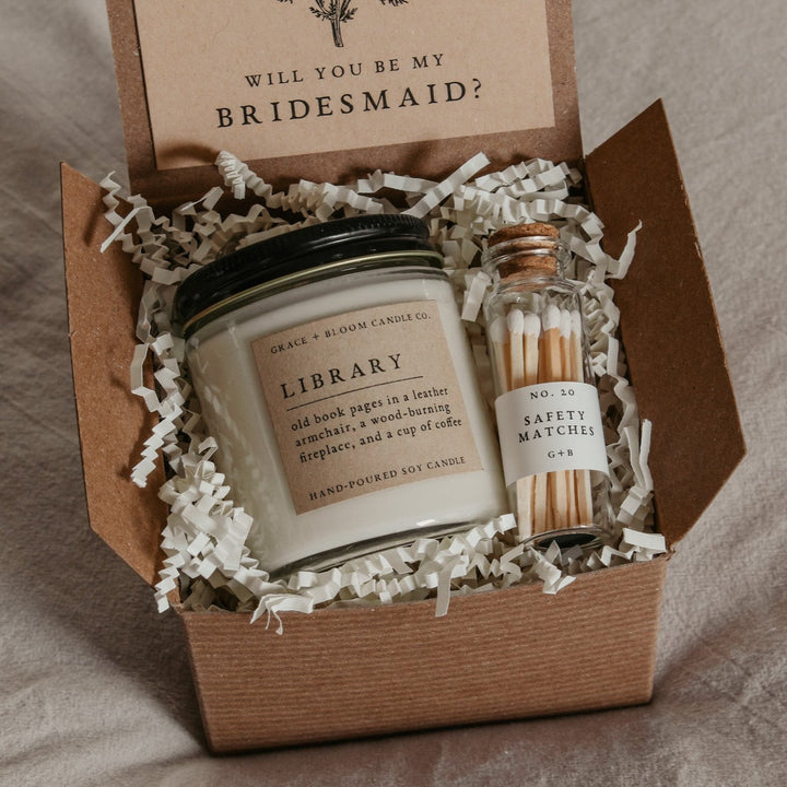 A cozy gift box with a candle in your choice of literary scents, a glass bottle of matches, and a kraft-colored card with a floral design and your choice of messages on it.