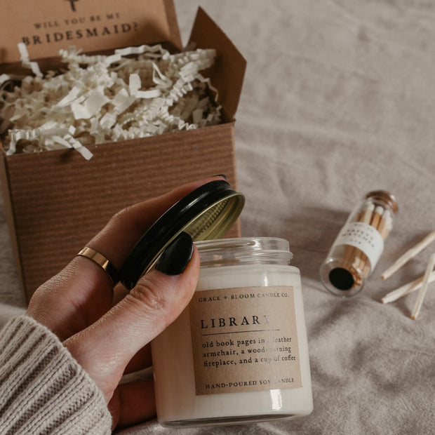 Give the gift of coziness with a boxed birthday gift from Grace and Bloom Co! It includes a small candle in a literary book inspired scent and a glass cork-topped bottle of matches. A card that says Happy Birthday in a vintage botanical style is attached to the inside cover of the box. It can be removed and used as a bookmark.