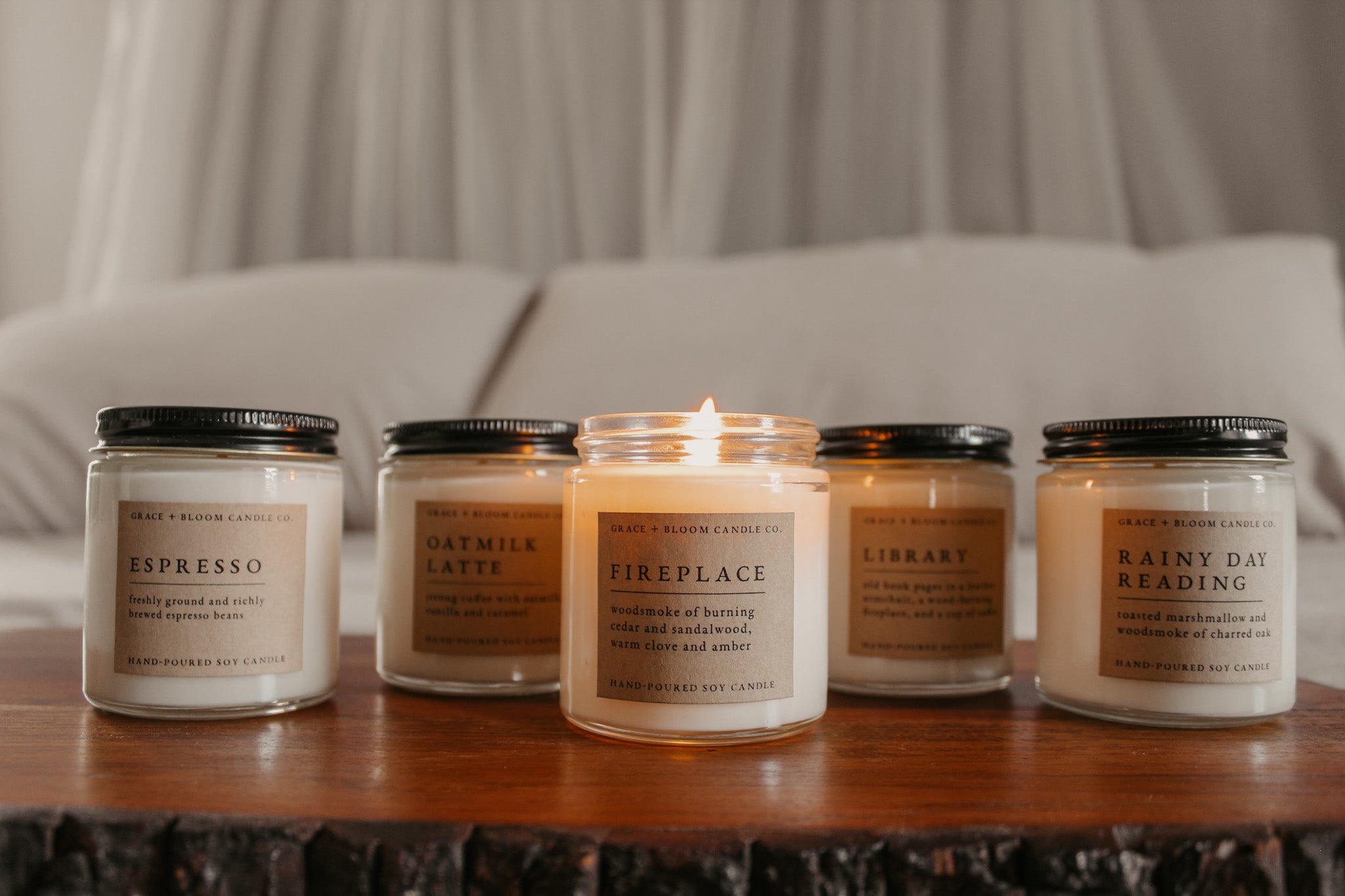 Five candles with labels on a wooden surface, with a neutral background.