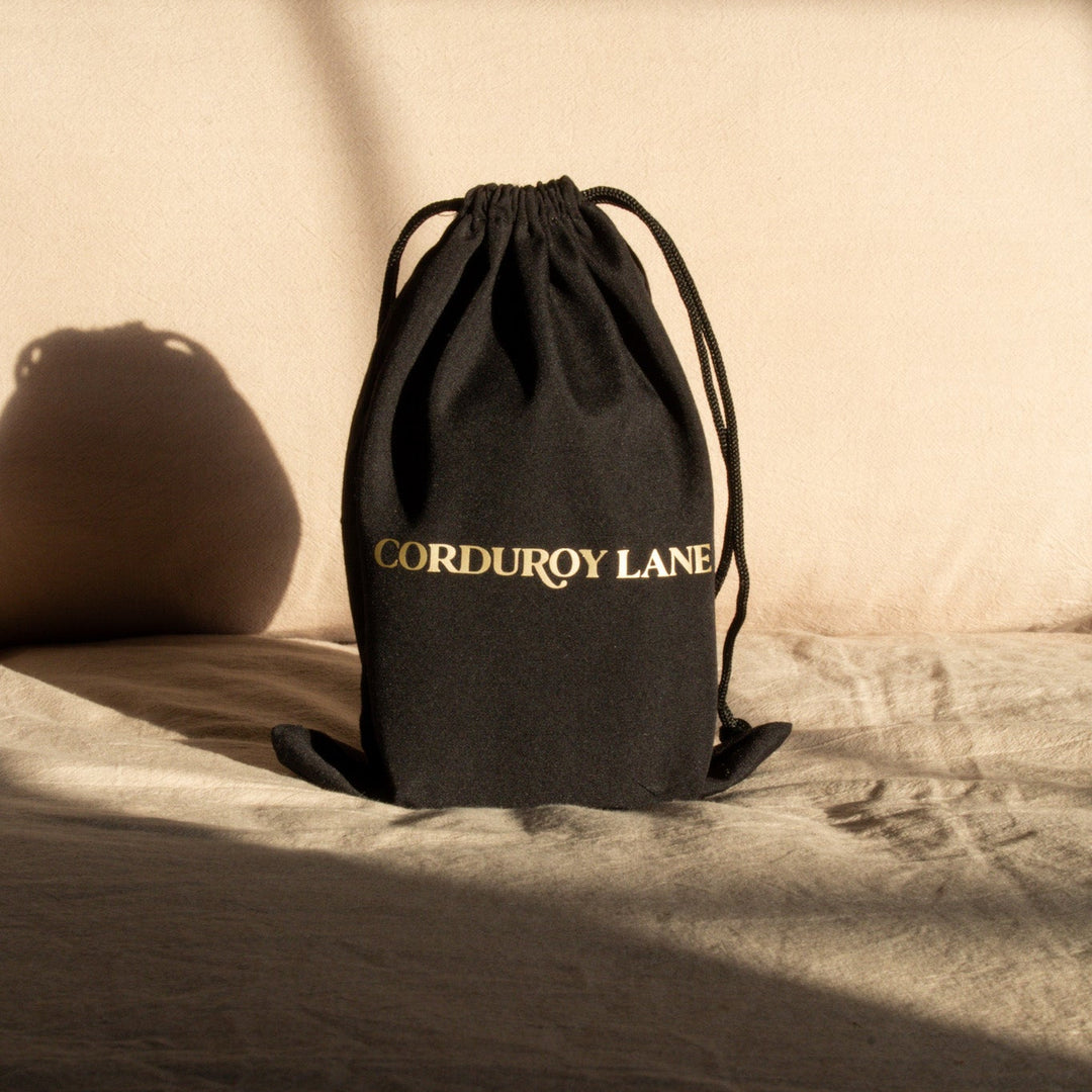 Black drawstring bag with 'Corduroy Lane' branding in gold lettering