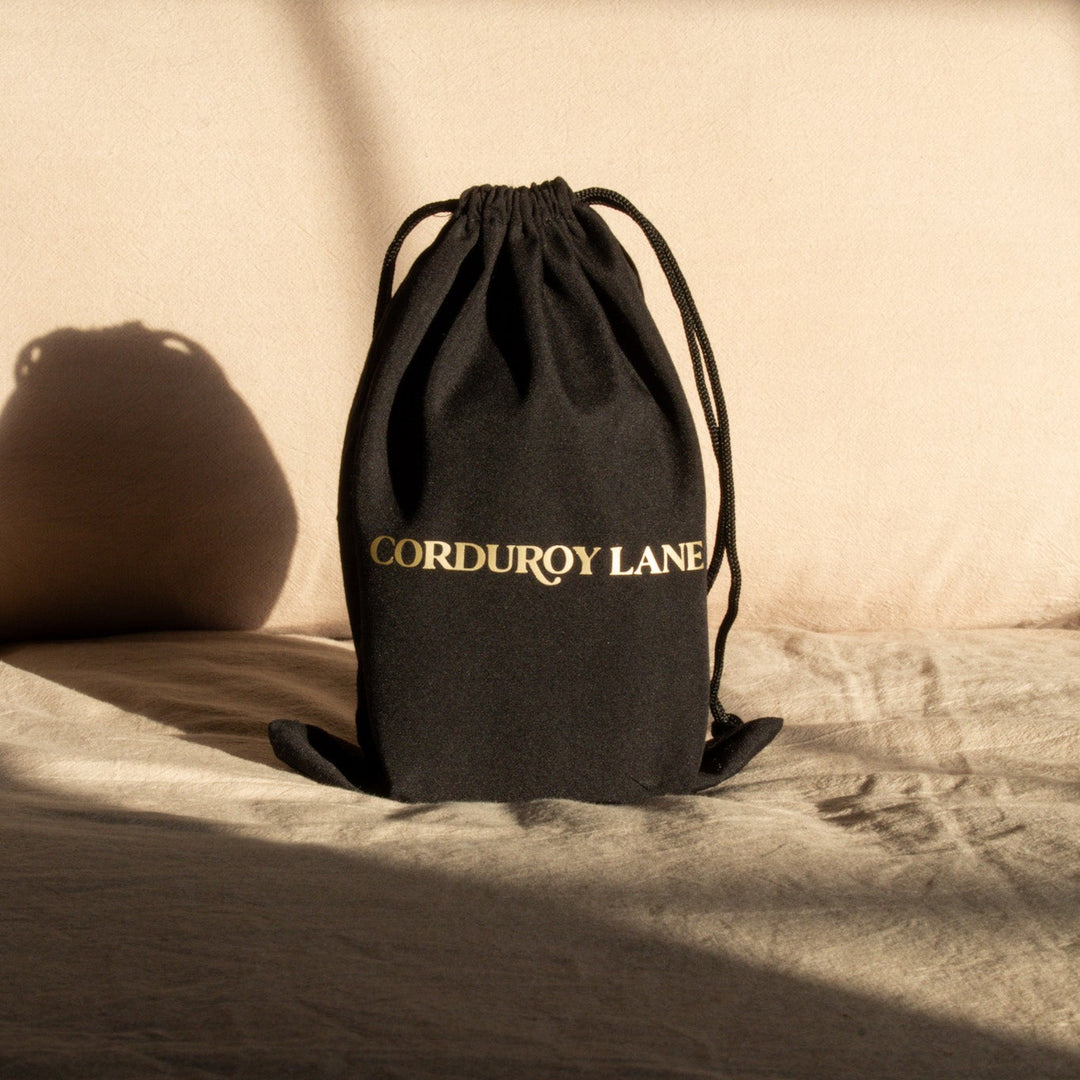 Black drawstring bag with 'Corduroy Lane' branding in gold lettering
