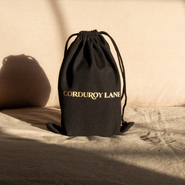 Black drawstring bag with 'Corduroy Lane' branding in gold lettering