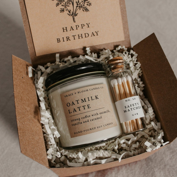 A cozy gift box from Corduroy Lane, perfect for bookish friends, has a candle in your choice of literary scents, a glass bottle of matches, and has a removable kraft-colored card with a floral design and your choice of messages on it.