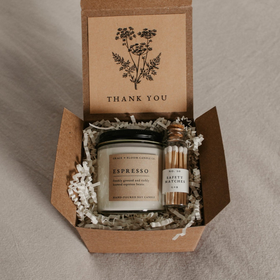 A cozy gift box with a candle in your choice of literary scents, a glass bottle of matches, and a kraft-colored card with a floral design and your choice of messages on it.