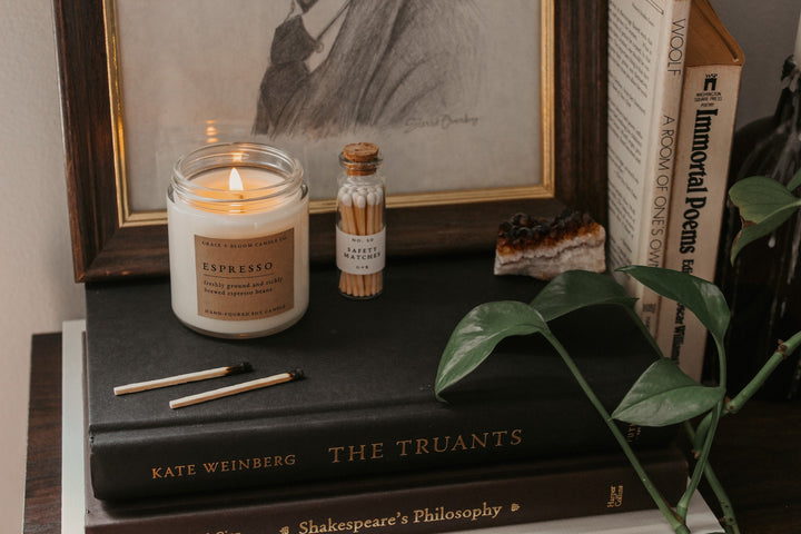 Candle on a stack of books with a framed picture and small bottle in the background