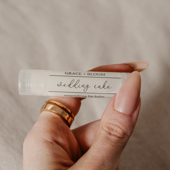 A hand holding a lip balm stick with clear caps, labeled with 'Wedding Cake'