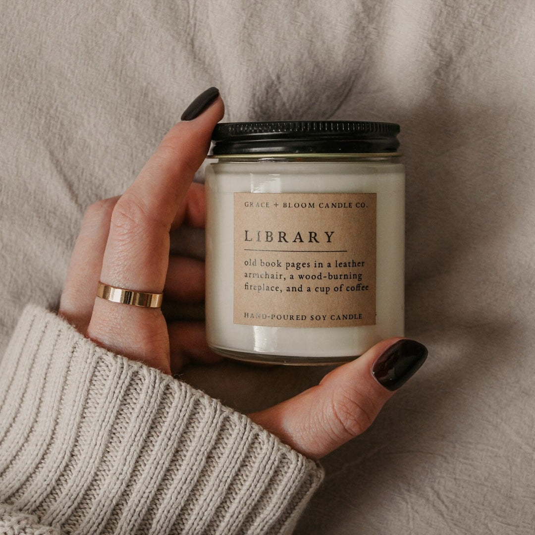 Hand holding a candle labeled 'Library' with a neutral background