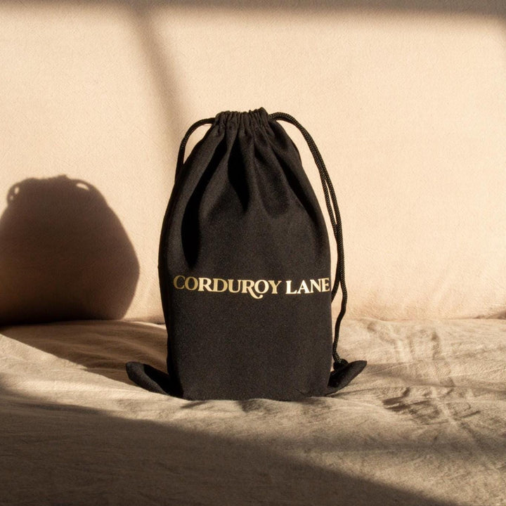 a black cotton gift bag with the words "Corduroy Lane" printed on it in gold