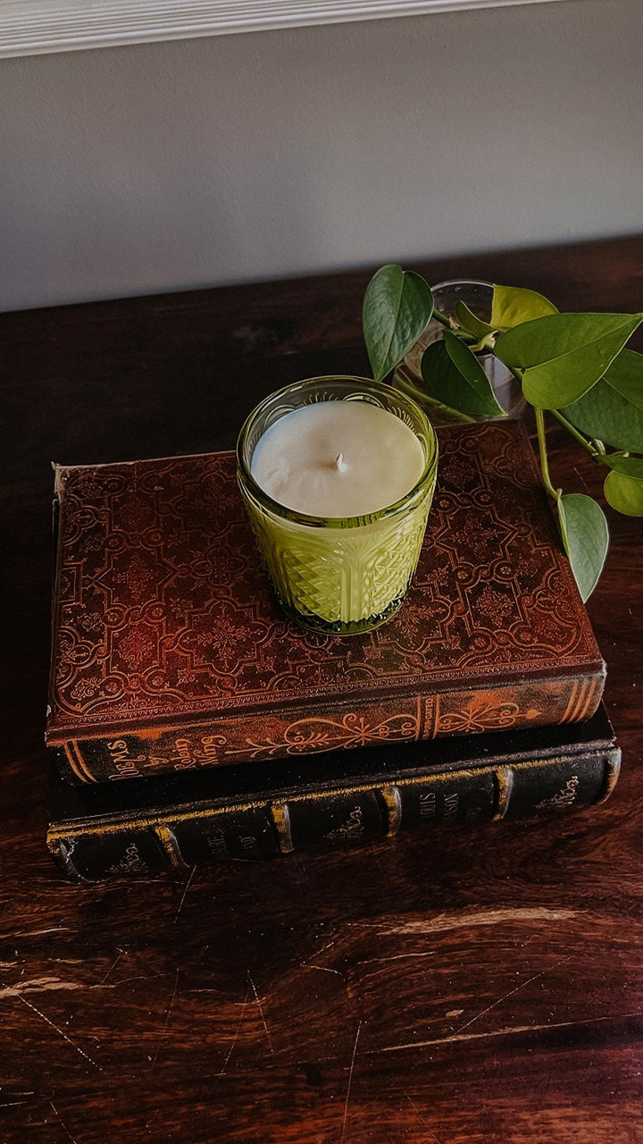 Garden Mint candle in a textured green glass holder on top of an old book with a plant in the background