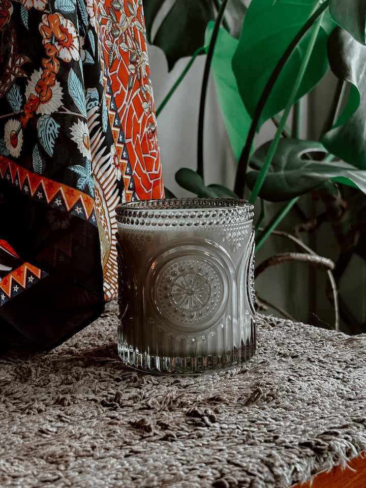 Decorative glass candle holder on a textured surface with a plant in the background