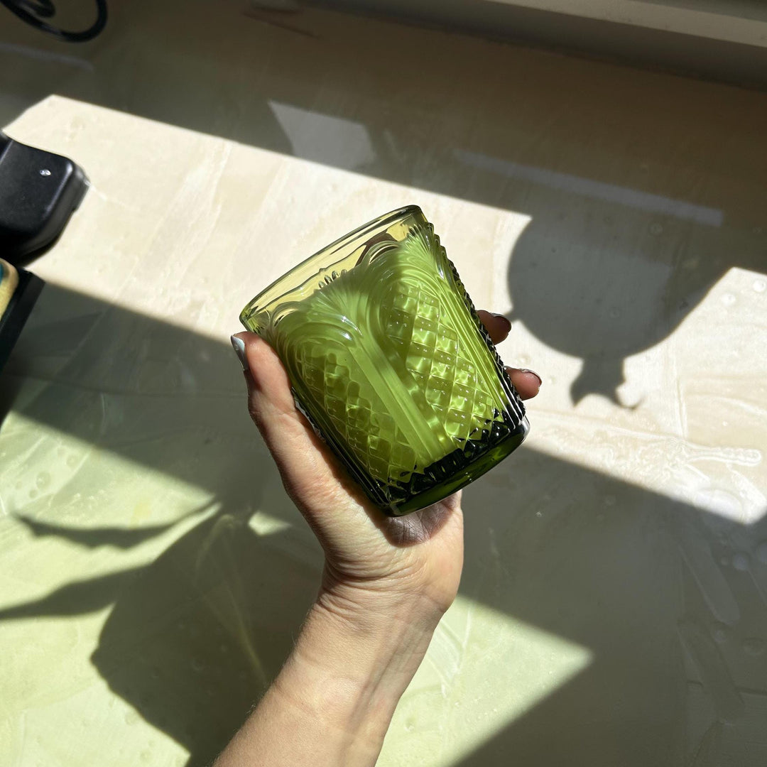 Hand holding a green textured glass container on a light surface
