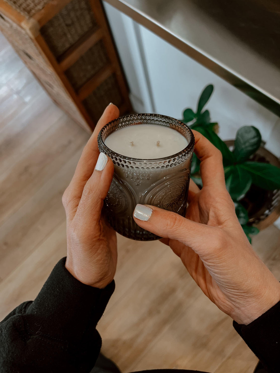 Person holding a Speakeasy candle in a textured glass holder indoors.