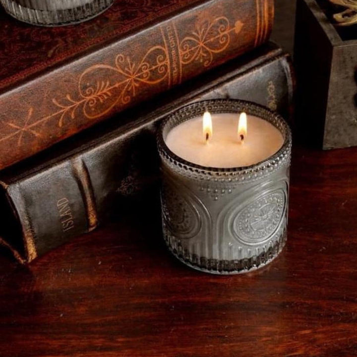 Candle in a decorative holder on a wooden surface with books in the background