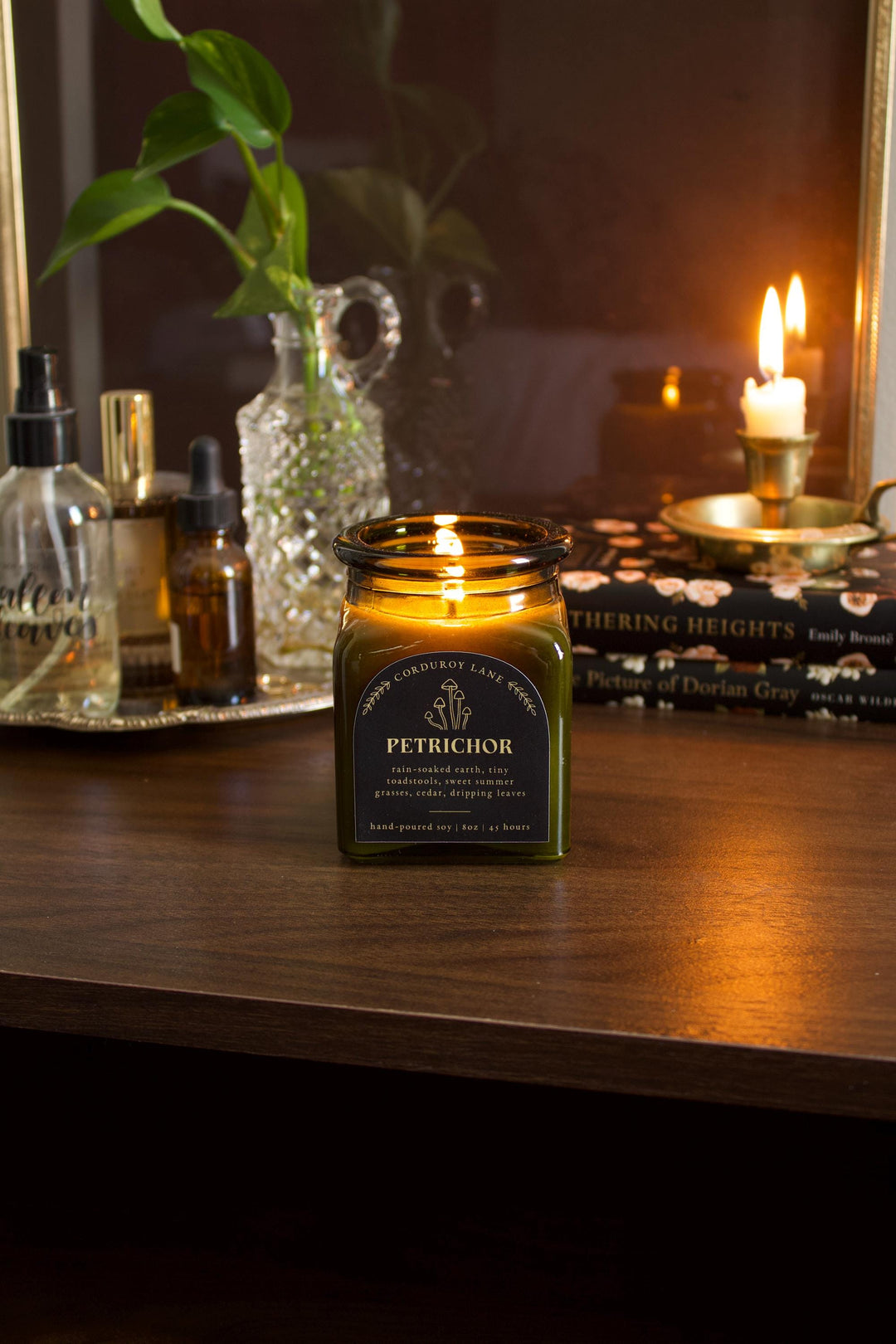 Candle in a green jar labeled 'Petrichor' on a wooden surface with a blurred background