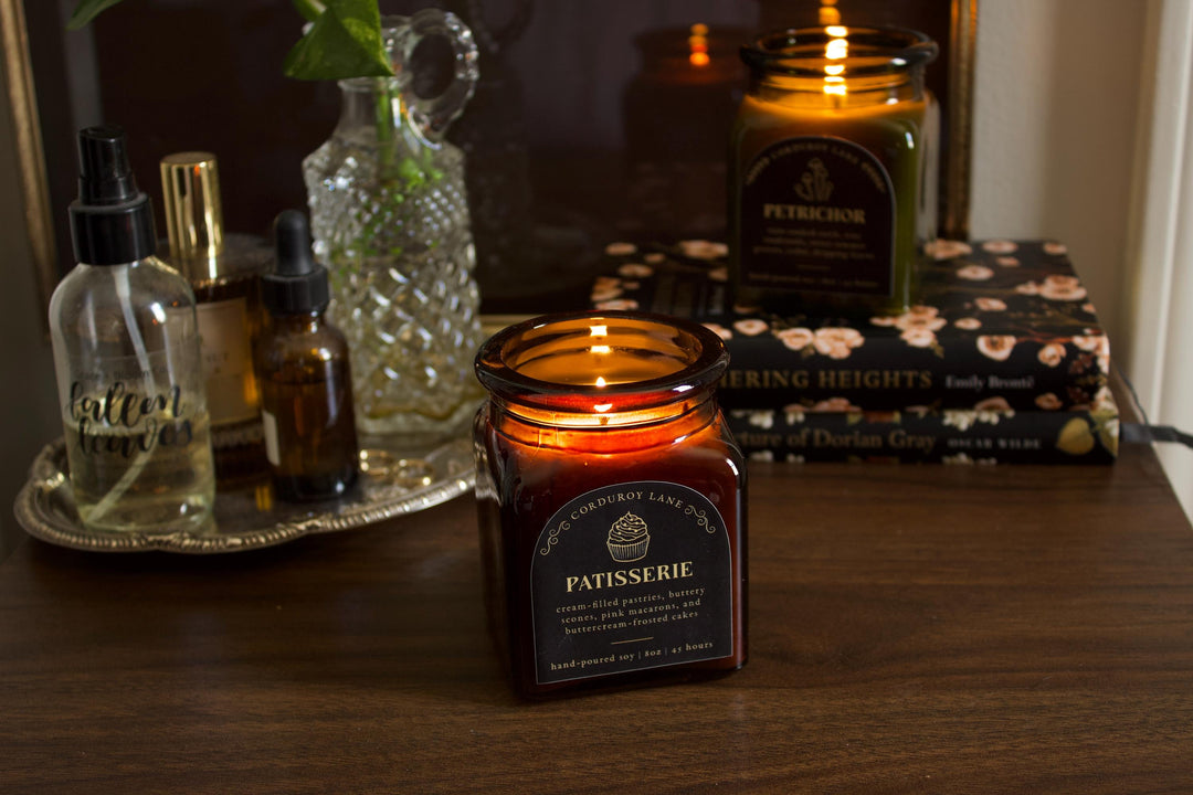 Candle labeled 'Patisserie' on a wooden surface with bottles and books in the background