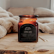 Library: a cozy apothecary candle from Corduroy Lane. A complex blend of old book pages, leather, woodsmoke, and coffee. An 8-oz amber glass jar with a cork lid a reusable black and gold cotton gift bag