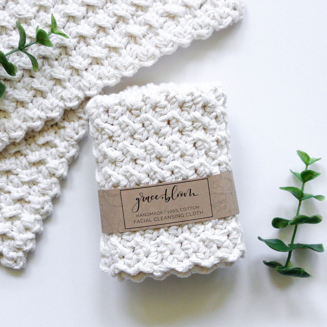 A cream-colored hand-crocheted 100% cotton facial cleansing cloth, folded and wrapped with a kraft paper label
